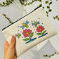 Beige pouch with colorful bee and flower design held by a hand against a light background.