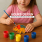 Child painting a dinosaur-shaped craft with colorful paint cans on a wooden table.