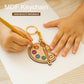 MDF keychain shaped like a paint palette with colorful dots and a brush, held by hands on a wooden surface.