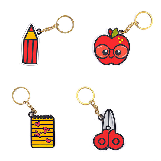 Four keychains shaped like a pencil, apple with glasses, notebook, and scissors on a white background.