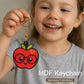 Child holding a red apple keychain with glasses, smiling.