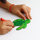 Child's hands holding a red marker and a green paper turtle on a white background